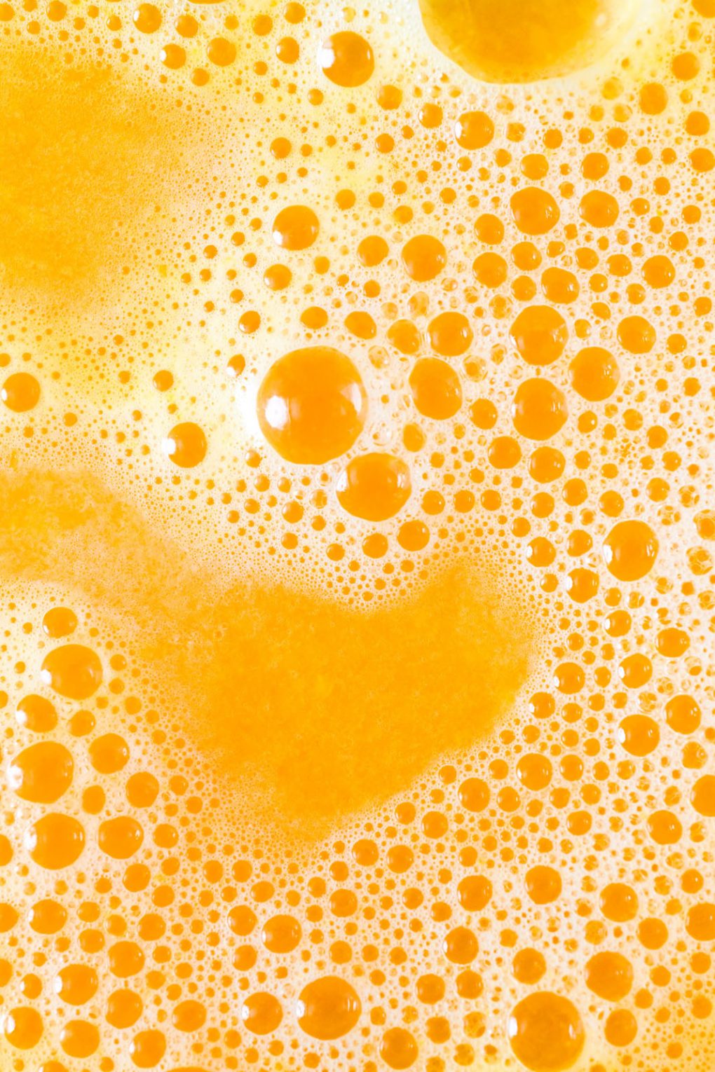 Close up macro shot bright orange wellness shot juice with bubbles on the surface. 