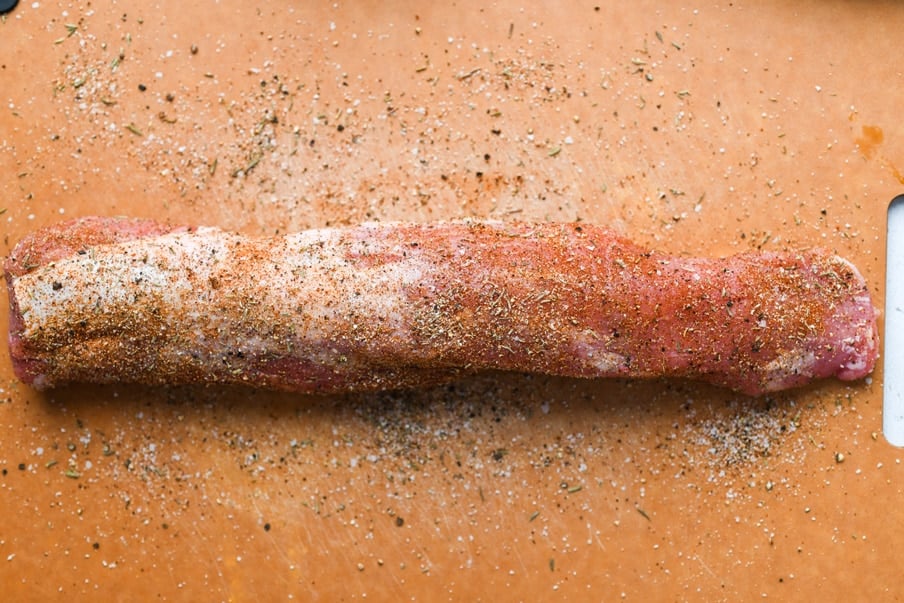 Overhead shot of a pork tenderloin covered in a spice rub, on a cutting board. 
