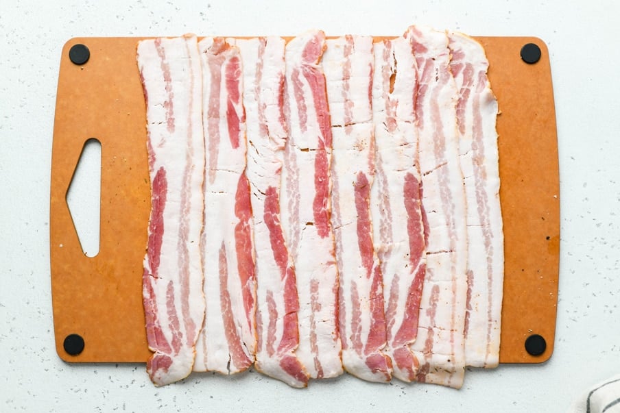 Overhead shot of bacon laid out in a rectangular shape on a cutting board. 