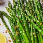 Roasted asparagus spears on a white plate with lemon wedges.