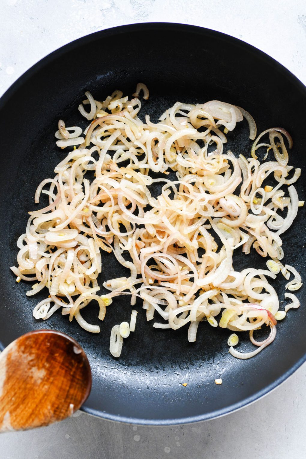 Overhead shot of a medium sized non stick skillet filled with caramelized thinly sliced shallots. On a light colored background. 