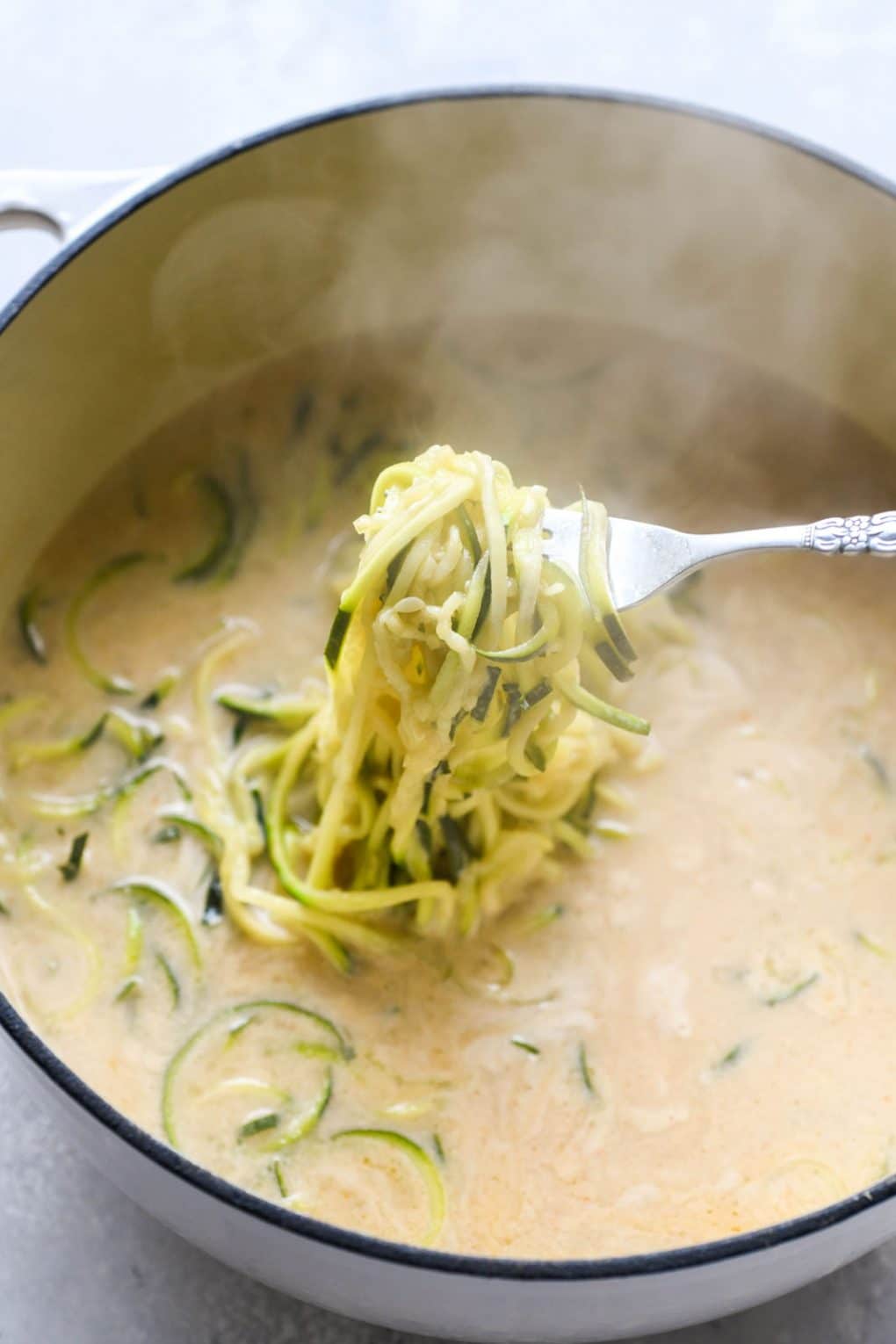 A fork pulling cooked zucchini noodles out of the steaming coconut broth. 
