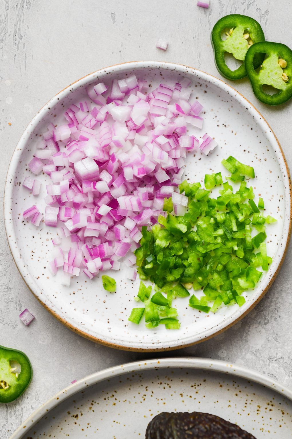 Close up image of a small white speckled plate with finely diced red onion and jalapeno. On a light grey background.
