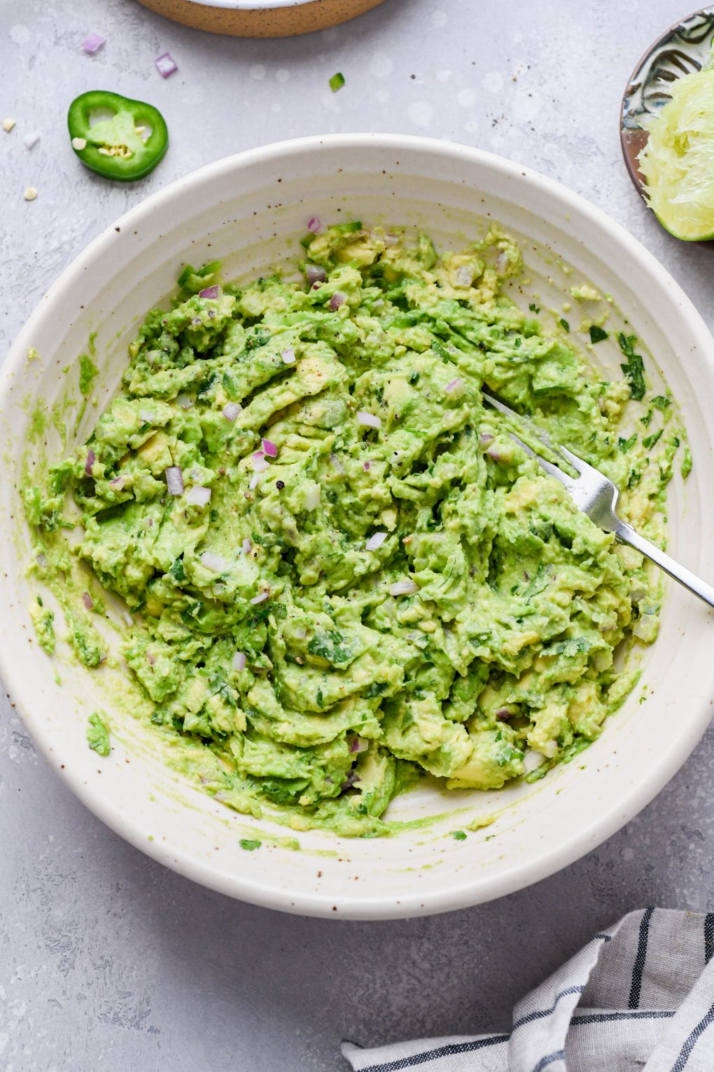 Image of easy guacamole smashed together with the other ingredients. On a light grey background. 