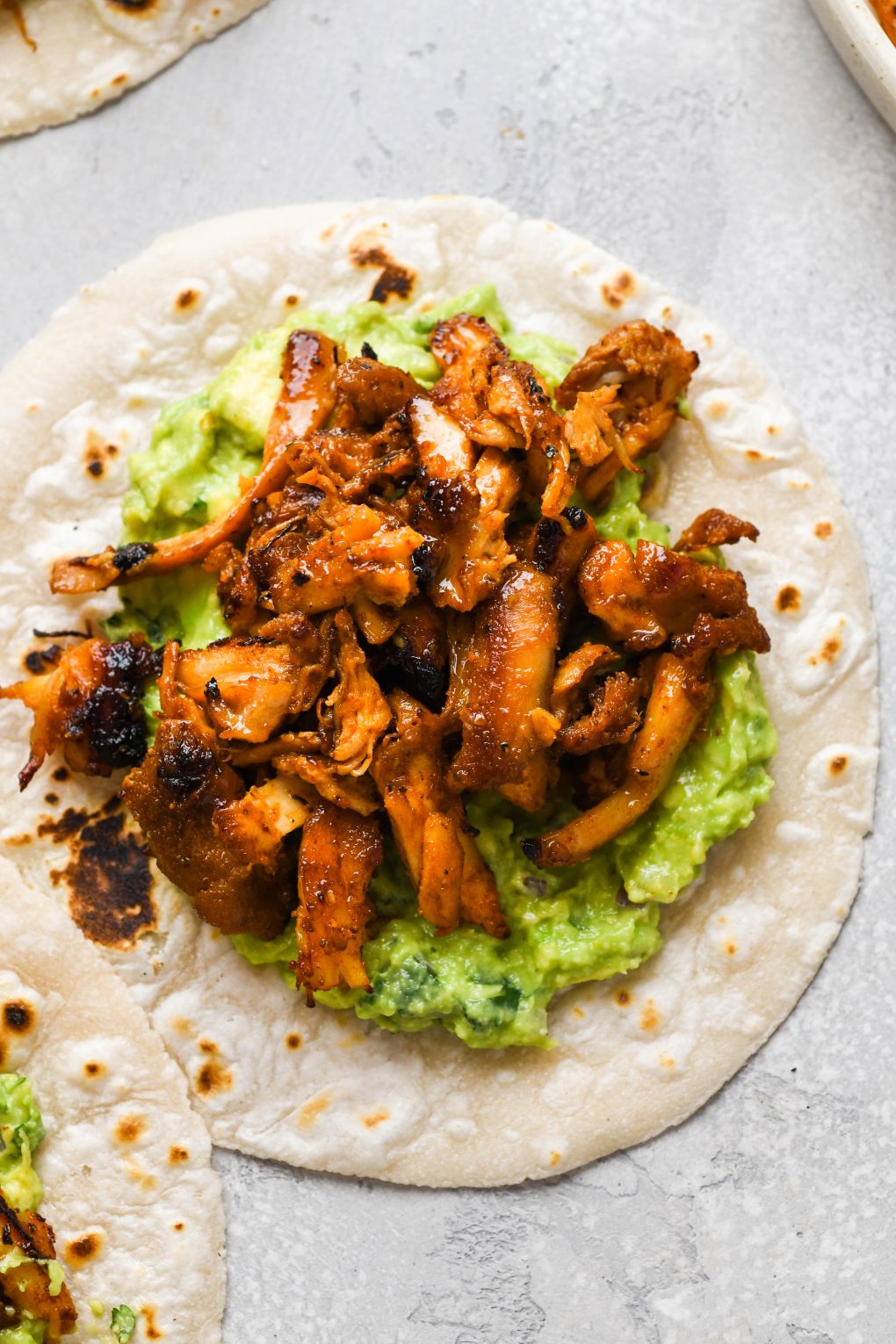 Close up image of a charred tortilla with guacamole and crispy seasoned shredded chicken.