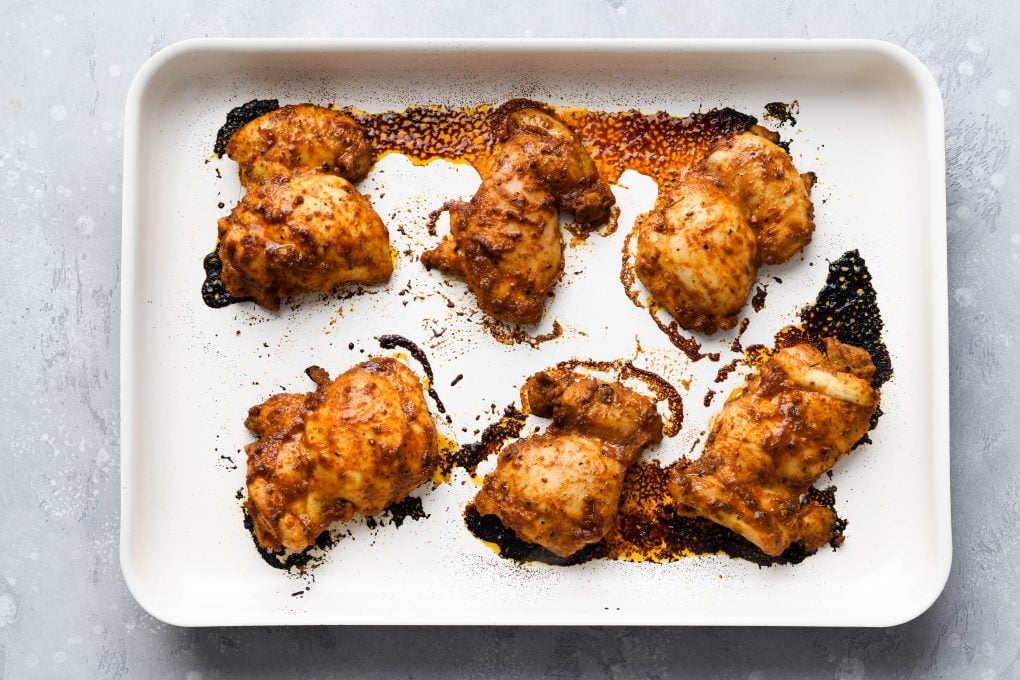 Overhead image of 6 cooked marinated chicken thighs on a light colored baking sheet
