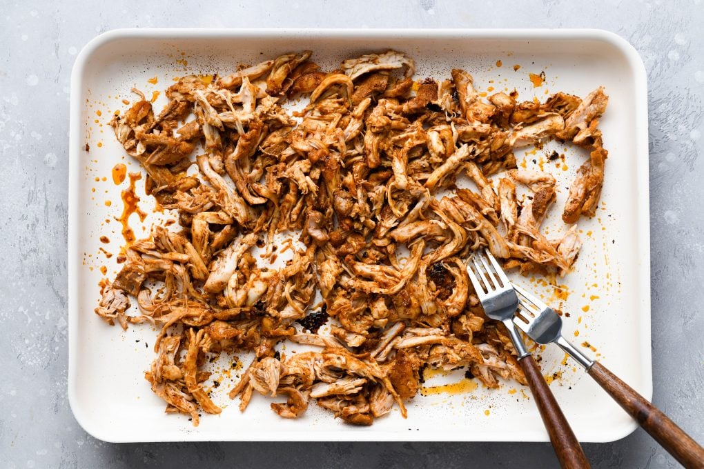 Overhead image of shredded chicken thighs on a light colored baking sheet