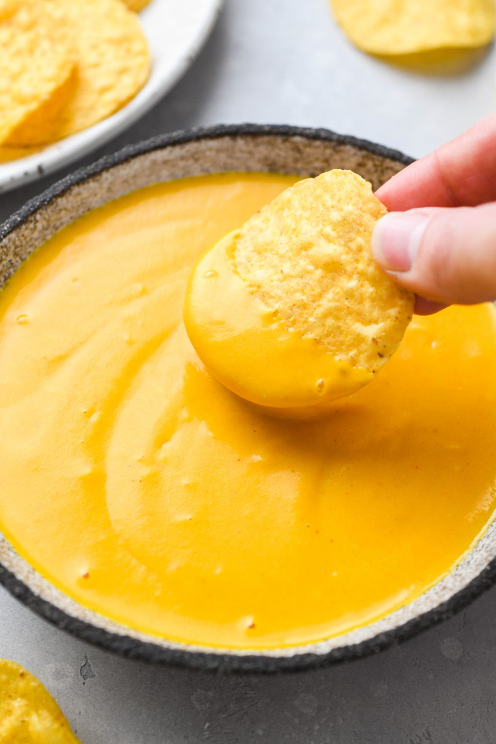 Image of a hand dipping a tortilla chip into a bowl of creamy vegan cheese sauce.