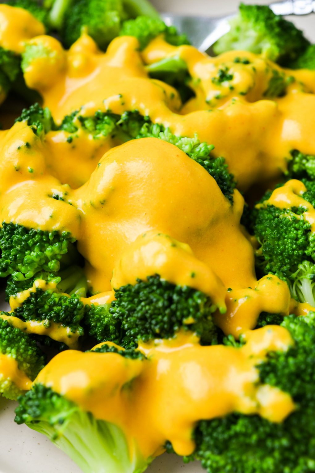 Close up image of cheese sauce drizzled over broccoli florets.