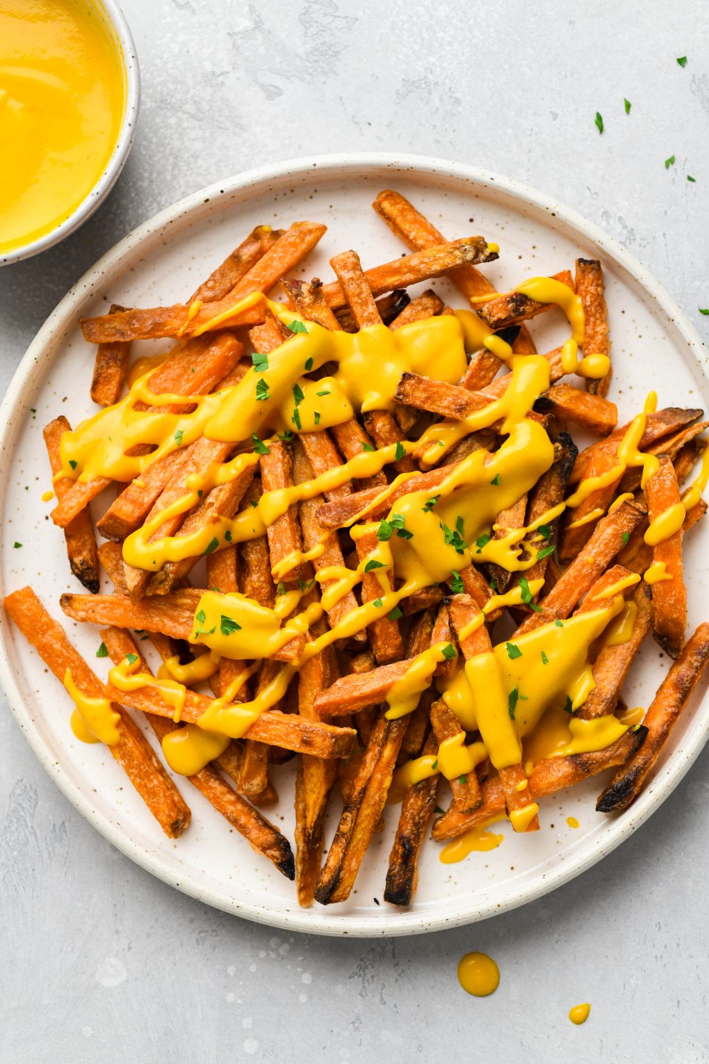 Image of cheese sauce drizzled over sweet potato fries on a white speckled plate.