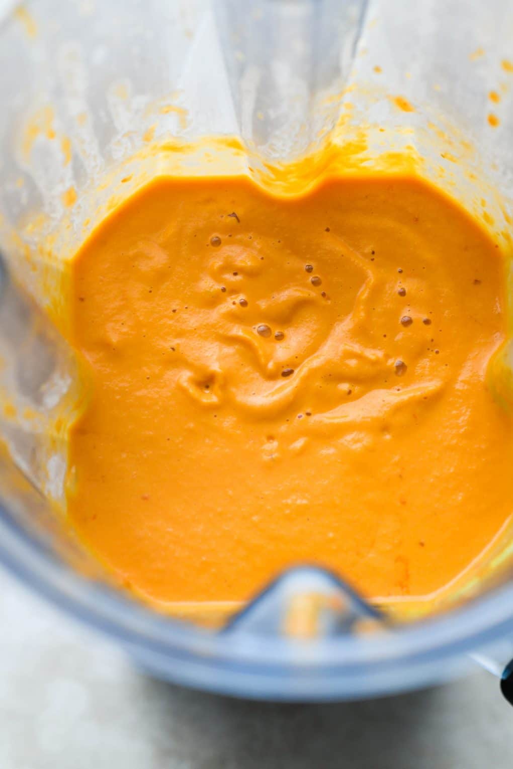 Close up shot of a bright orange creamy vegan vodka sauce inside a blender container.