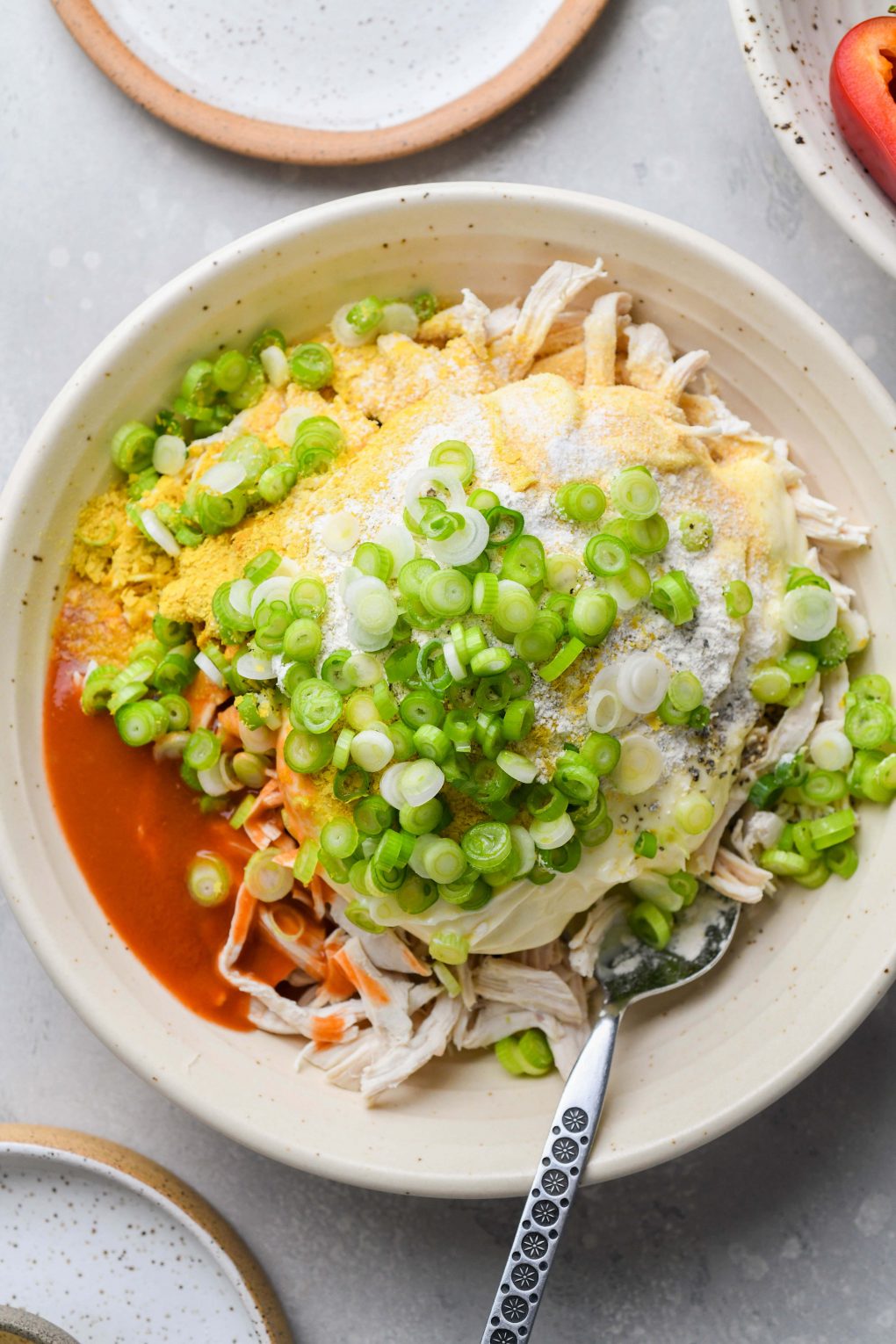 Image of a large bowl filled with the ingredients for buffalo shredded chicken - shredded chicken, mayo, green onions, hot sauce, and spices.