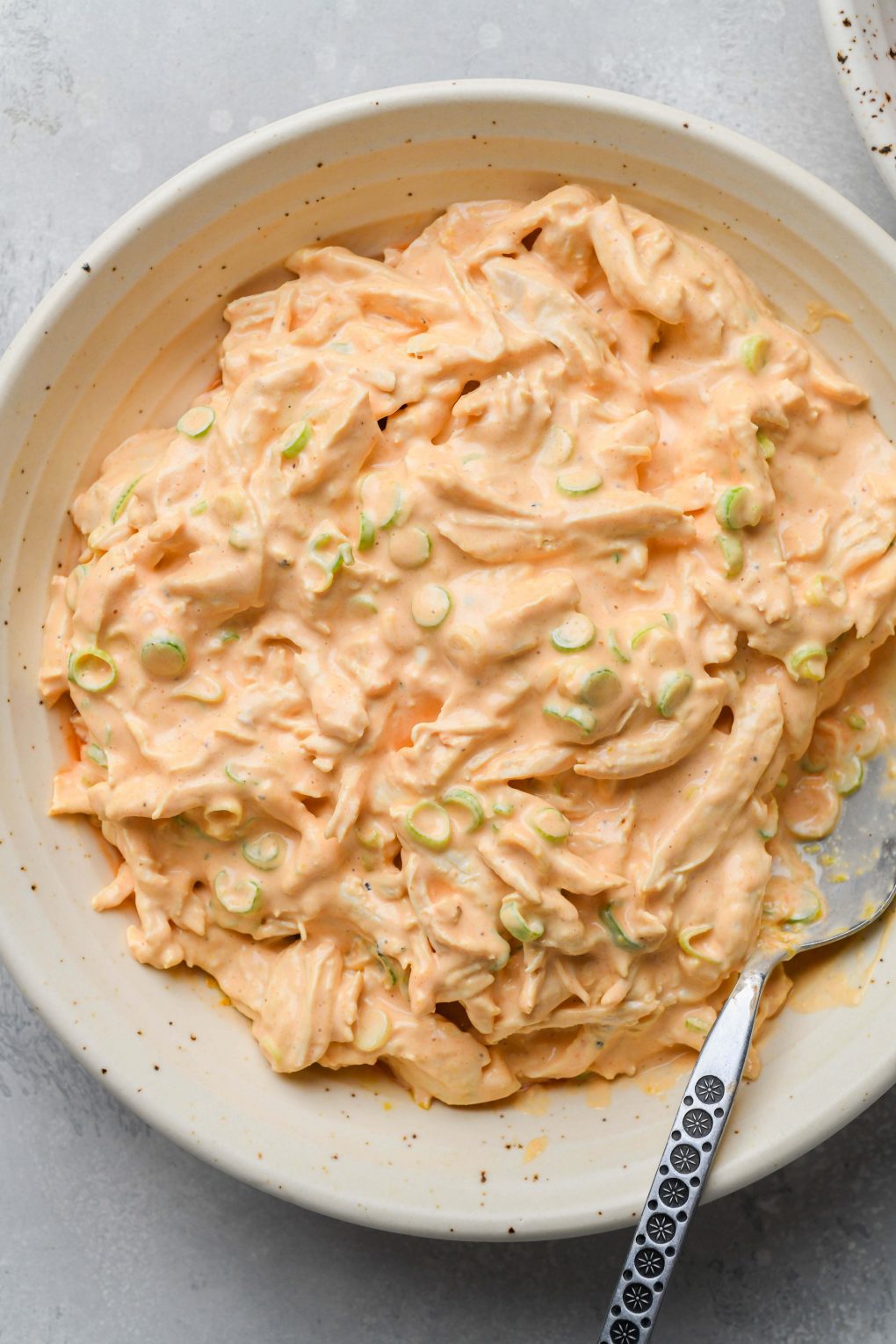 Image of a large bowl filled with the ingredients for buffalo shredded chicken all mixed together- shredded chicken, mayo, green onions, hot sauce, and spices.