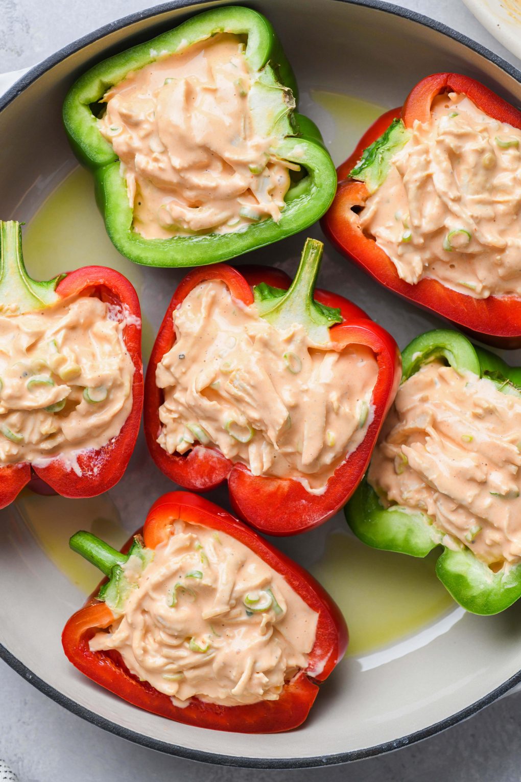 Raw bell peppers filled with shredded buffalo chicken mixture in an enameled white skillet.