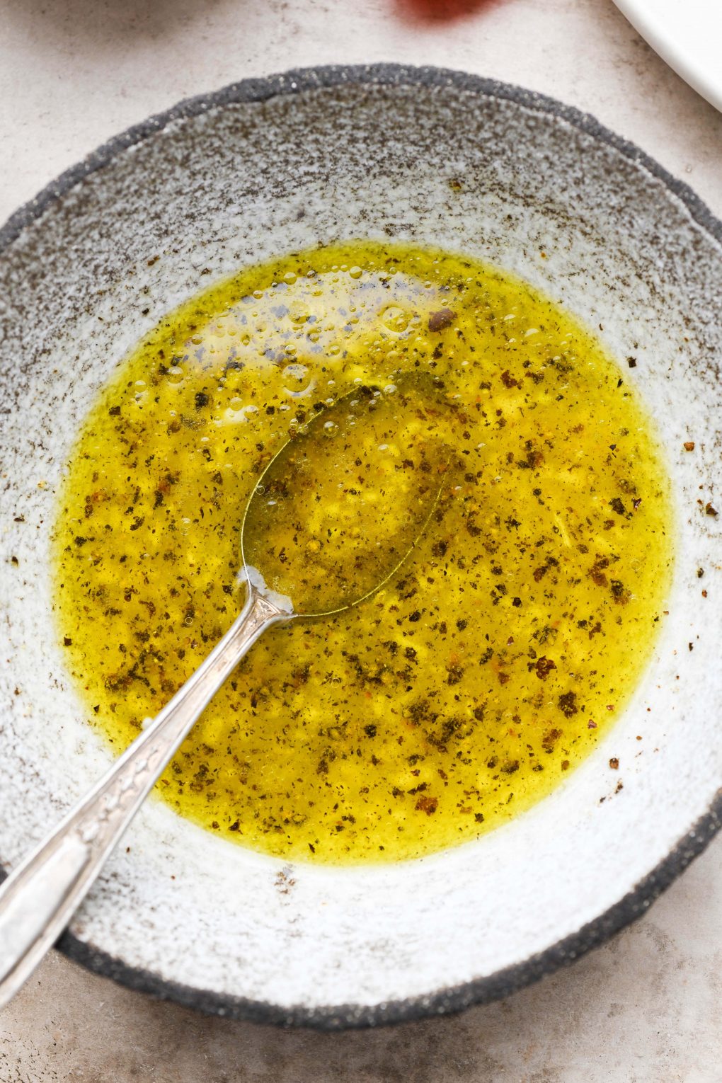 Close up of a small textured bowl filled with the ingredients for the lemony salad dressing whisked together.