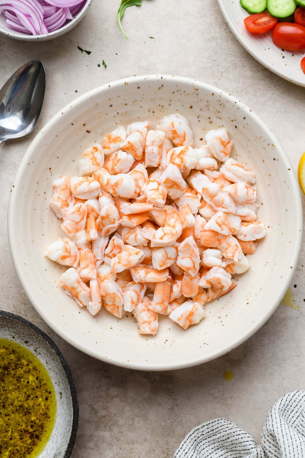 Image of a large speckled bowl of cooked shrimp without tails, cut into thirds.