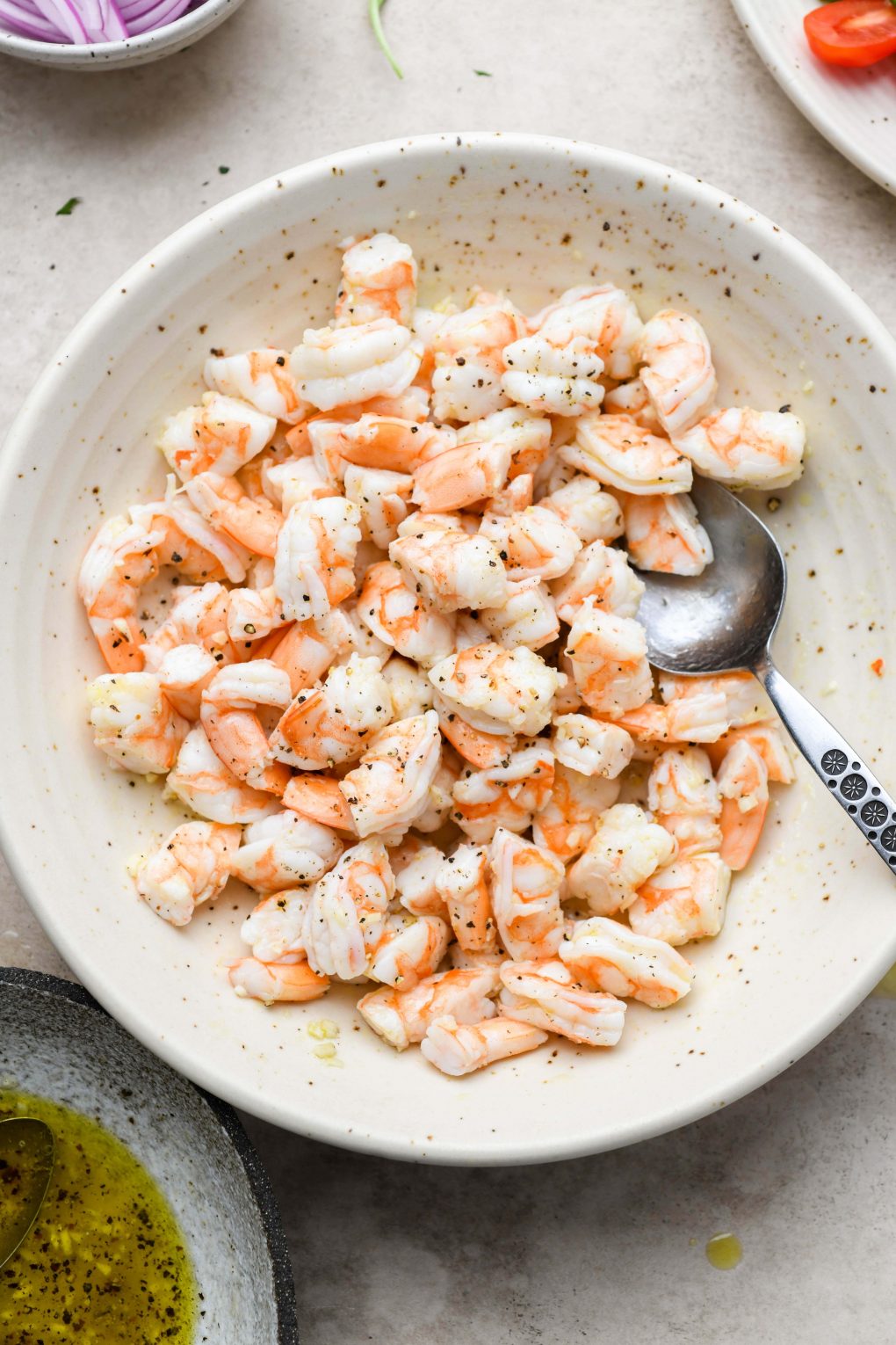 Image of a large speckled bowl of cooked shrimp without tails, cut into thirds and tossed with a bit of the lemony dressing. 