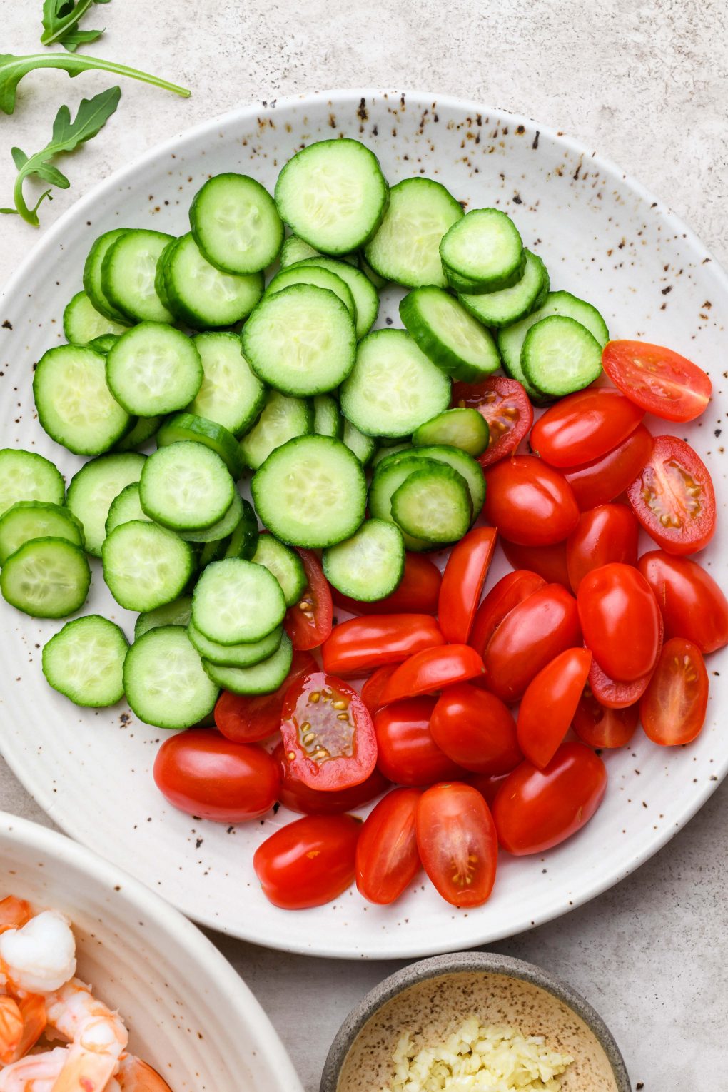 A large plate filled with sliced cucumber and sliced cherry tomatoes on a light beige background. 