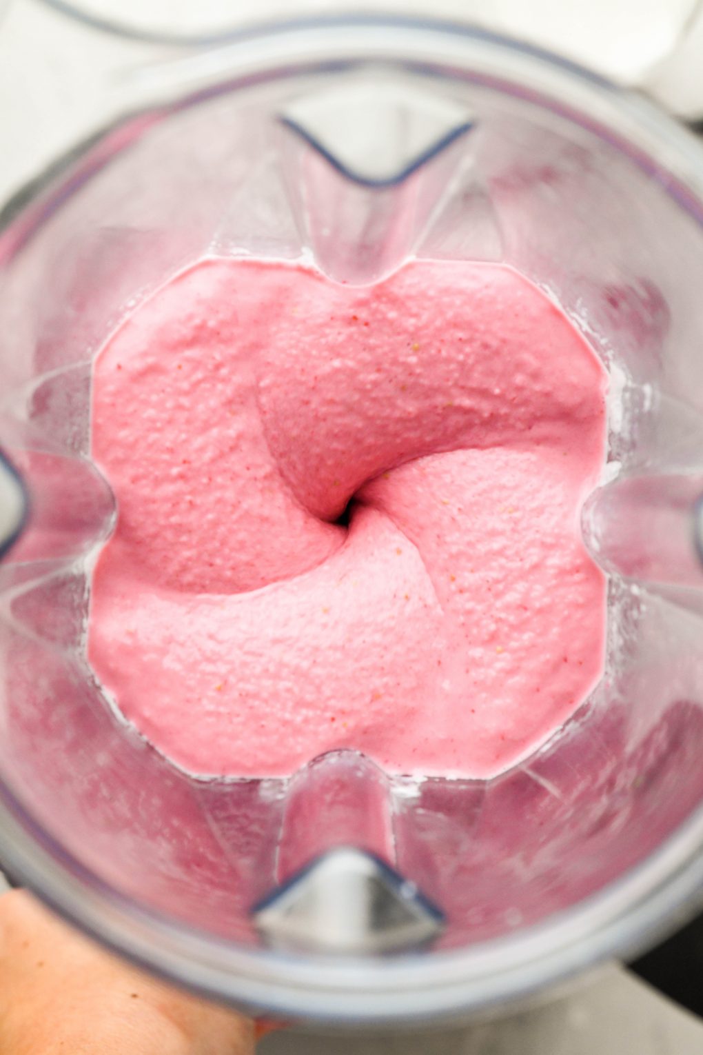 Overhead shot of the interior of a blender container blending a thick and creamy strawberry banana smoothie. 