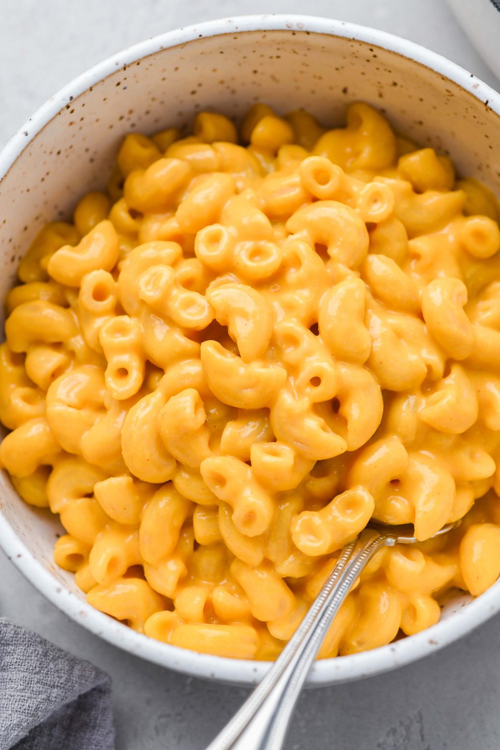 Close up image of a white speckled bowl filled with bright orange creamy vegan mac and cheese
