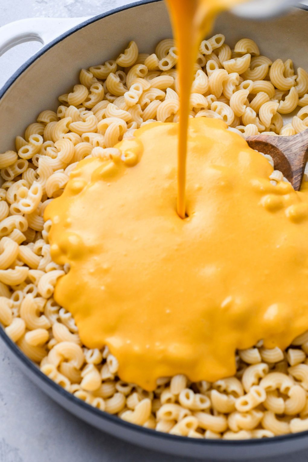 Close up shot of creamy vegan cheese being poured into a large skillet of cooked macaroni pasta.