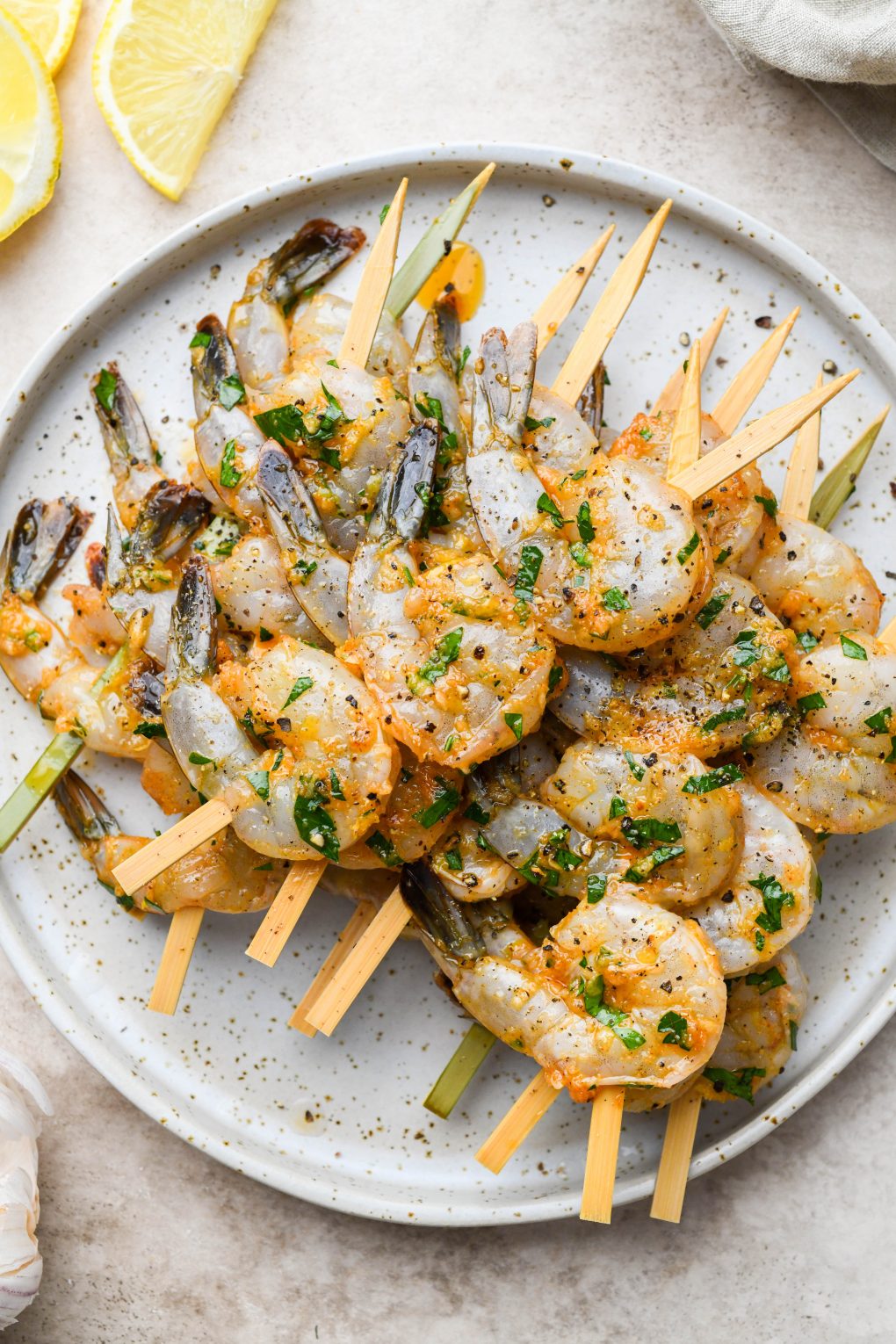 Overhead image of marinated shrimp threaded onto short wooden bamboo skewers. On a light colored speckled plate.