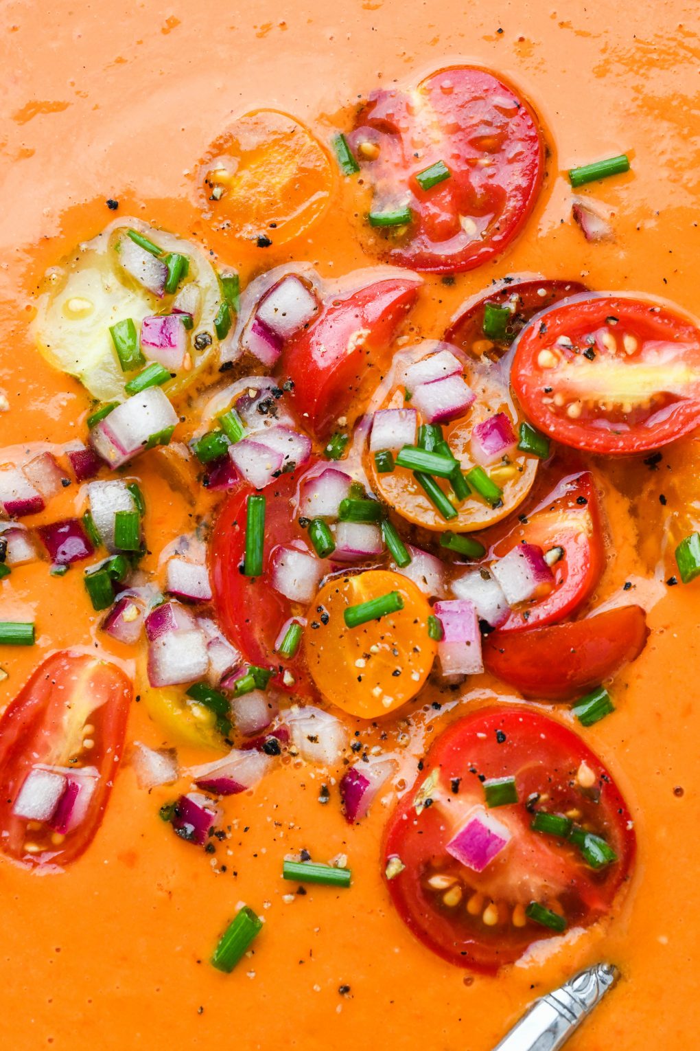 Close up of cherry tomato salad garnish on top of a bowl of bright orange gazpacho. 