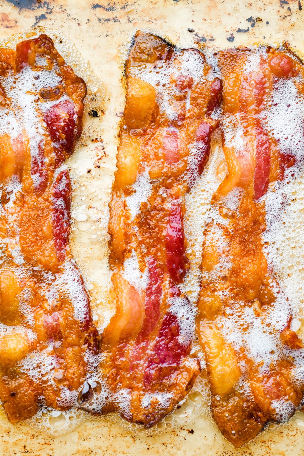 Close up of crispy golden brown strips of cooked bacon on a parchment lined baking sheet.