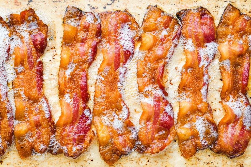 Crispy golden brown strips of cooked bacon on a parchment lined baking sheet.
