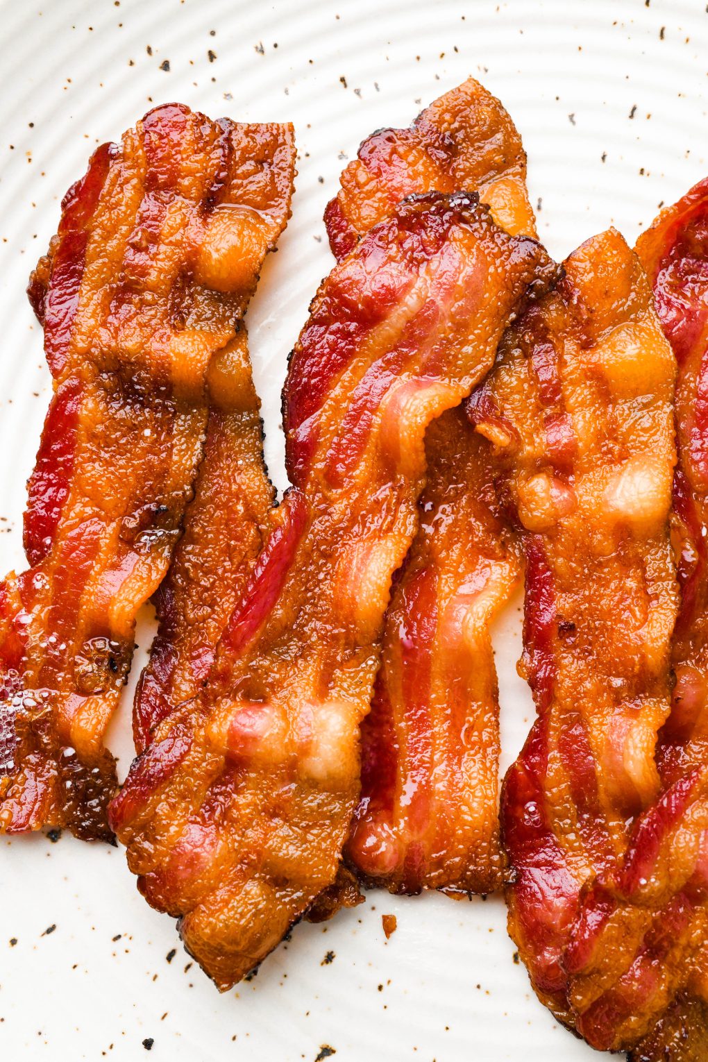 Crispy strips of bacon on a white speckled plate.