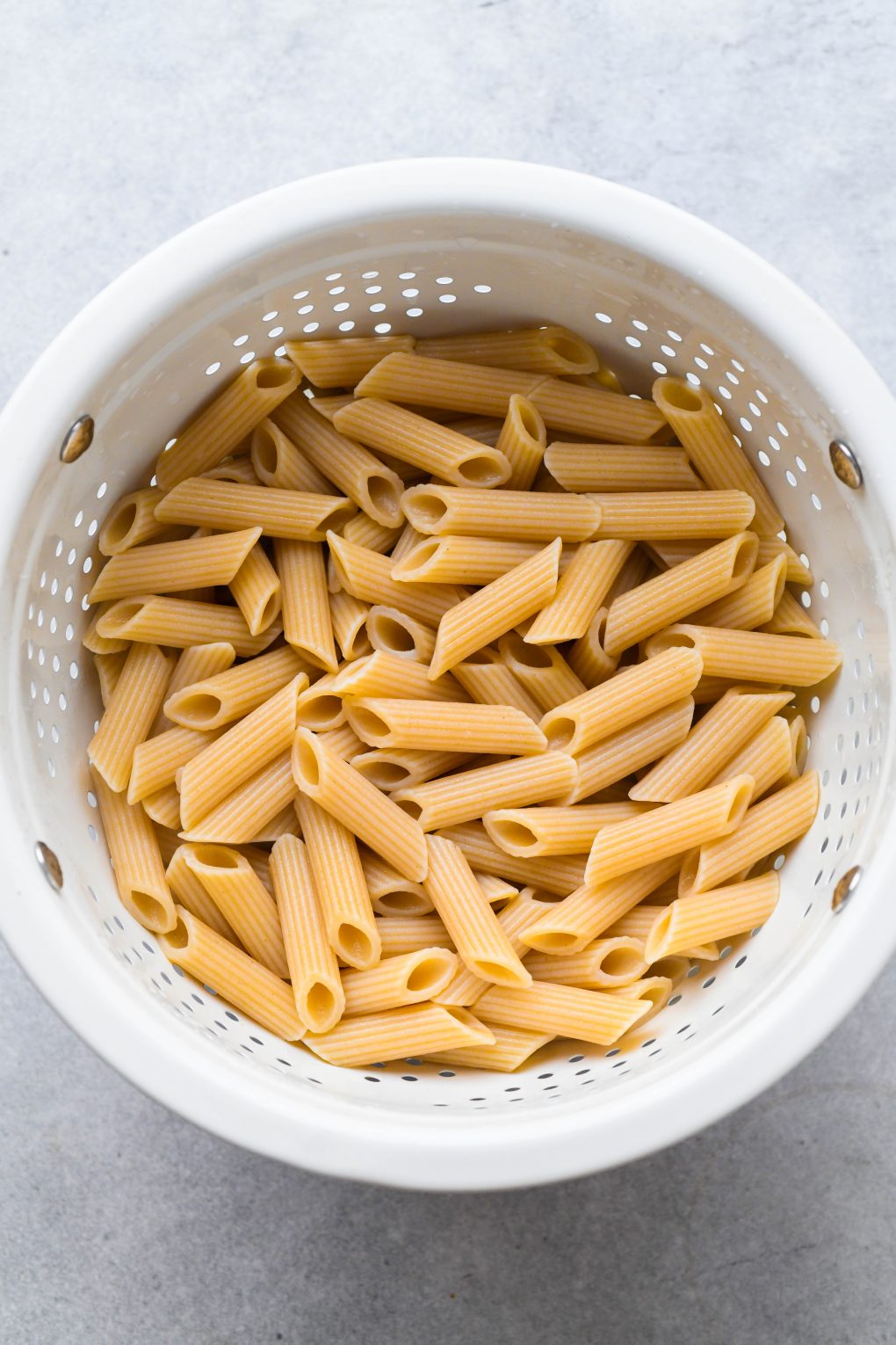 White colander with cooked gluten free penne pasta.