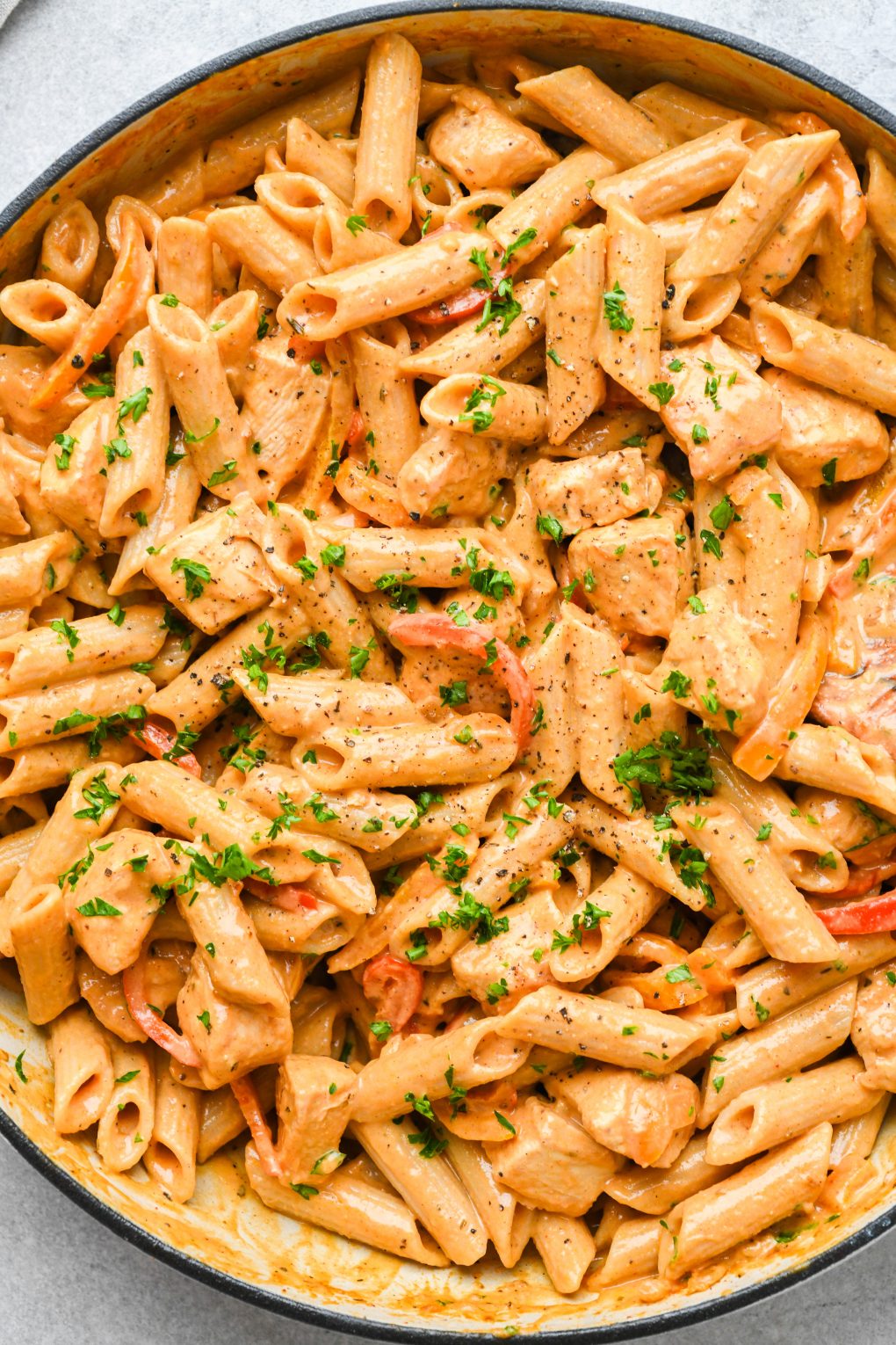 Close up image of a ceramic skillet filled with super creamy cajun chicken pasta. Topped with chopped parsley on a light colored background.