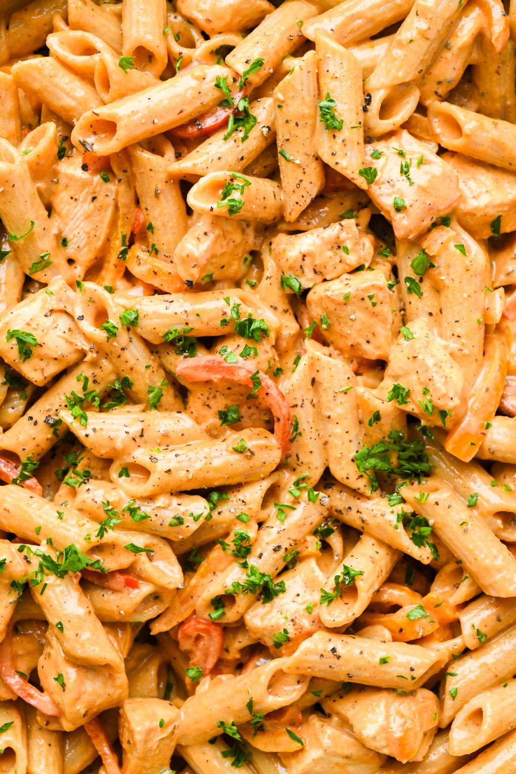 Close up macro style shot of creamy cajun chicken penne pasta topped with chopped parsley. 