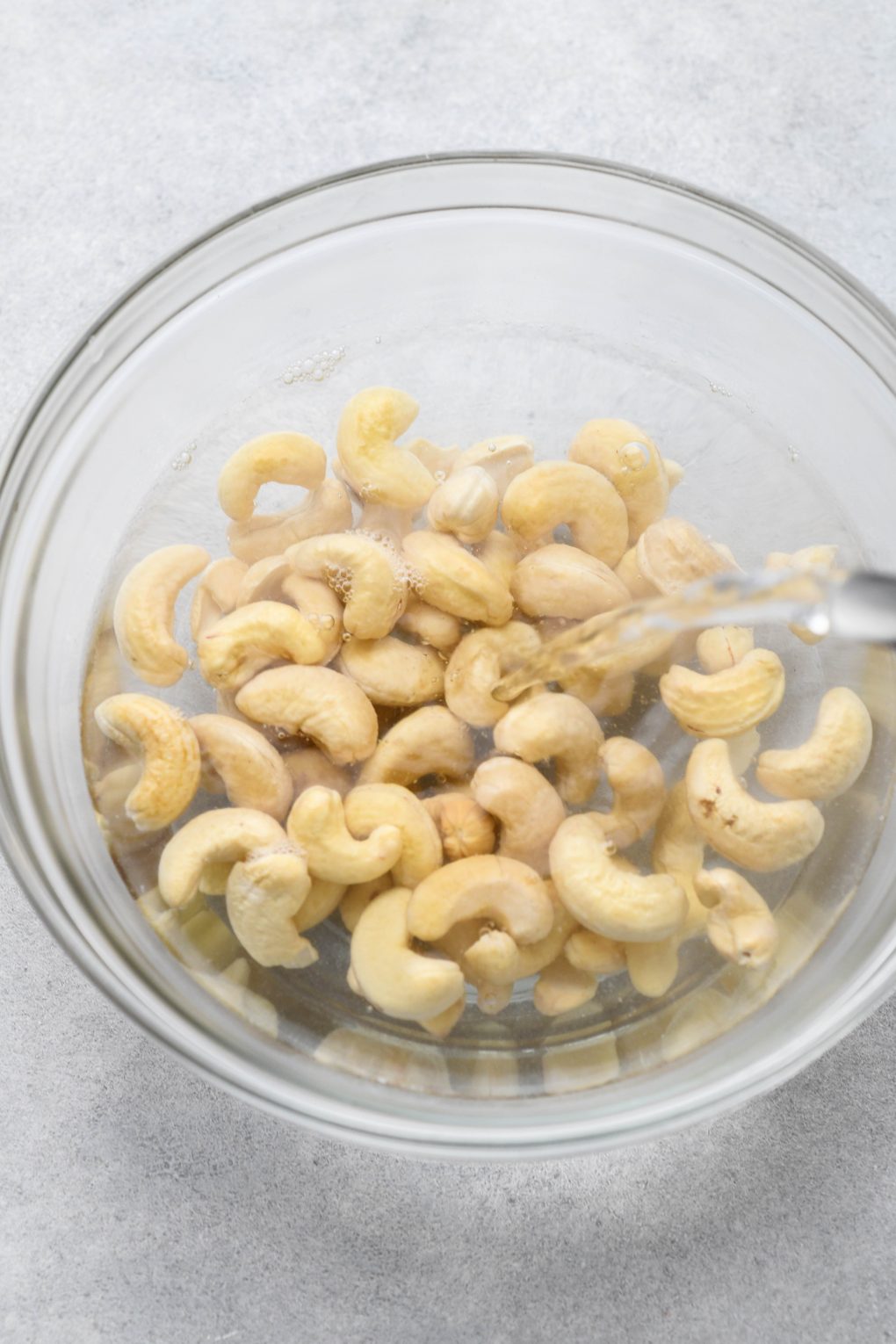 Raw cashews in a glass bowl being filled with hot water.