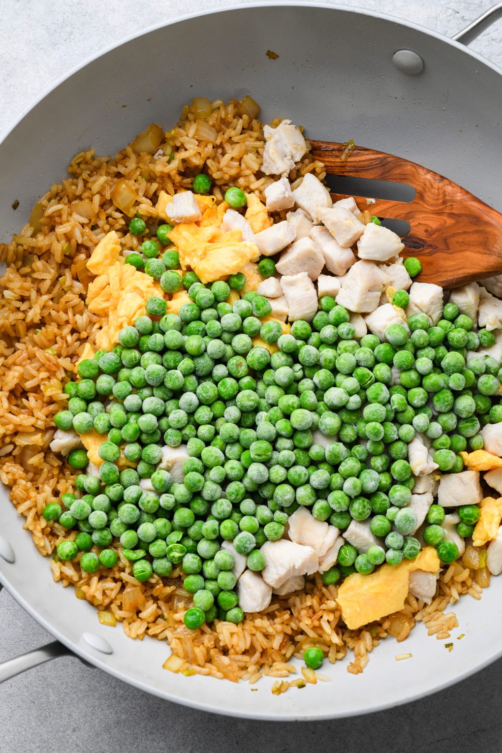 Wok with fried rice, cooked chicken, scrambled eggs, and frozen peas added.