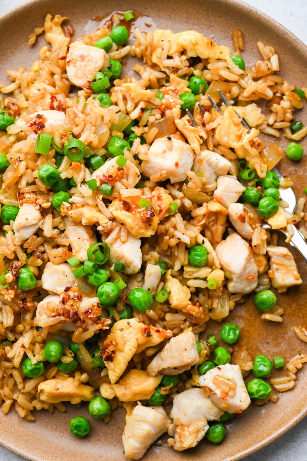 A plate of gluten free chicken fried rice garnished with green onions and chili oil, with  few bites taken out.