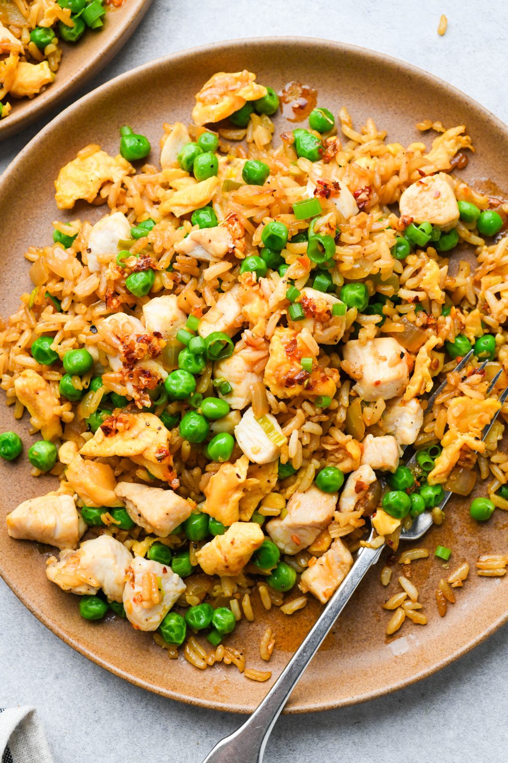 A plate of gluten free chicken fried rice garnished with green onions and chili oil.