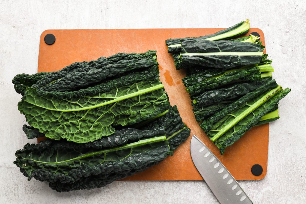 Whole kale leaves on a cutting board, with the tough end of the stems chopped off. 