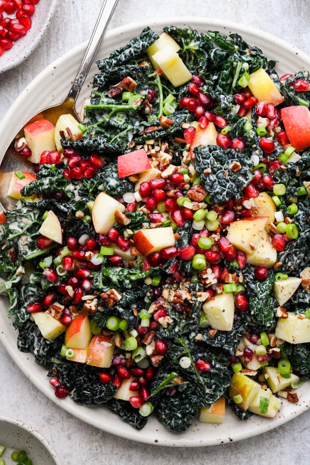 A large plate filled with colorful kale apple pomegranate salad with creamy tahini dressing.