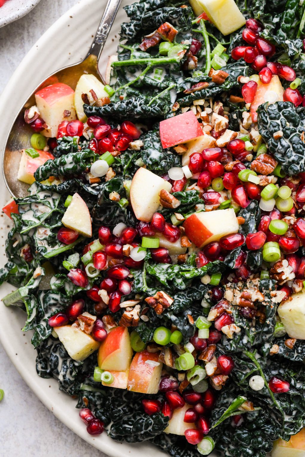 A large plate filled with colorful kale apple pomegranate salad with creamy tahini dressing.