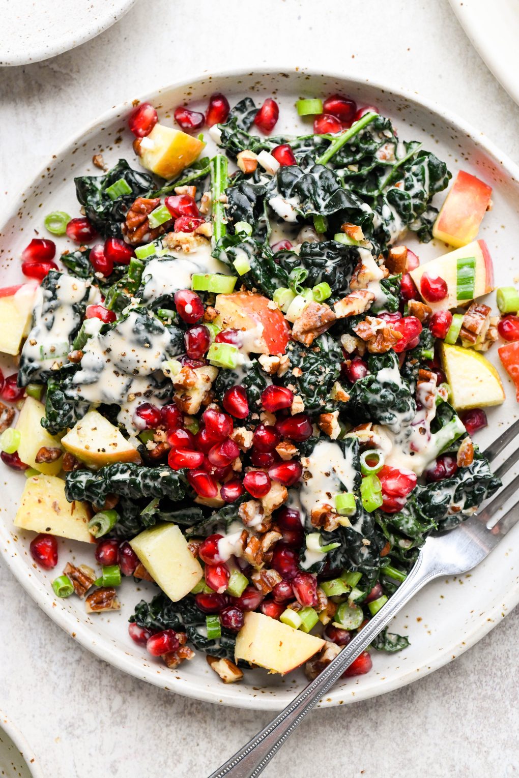 A small salad plate filled with colorful kale apple pomegranate salad with creamy tahini dressing.