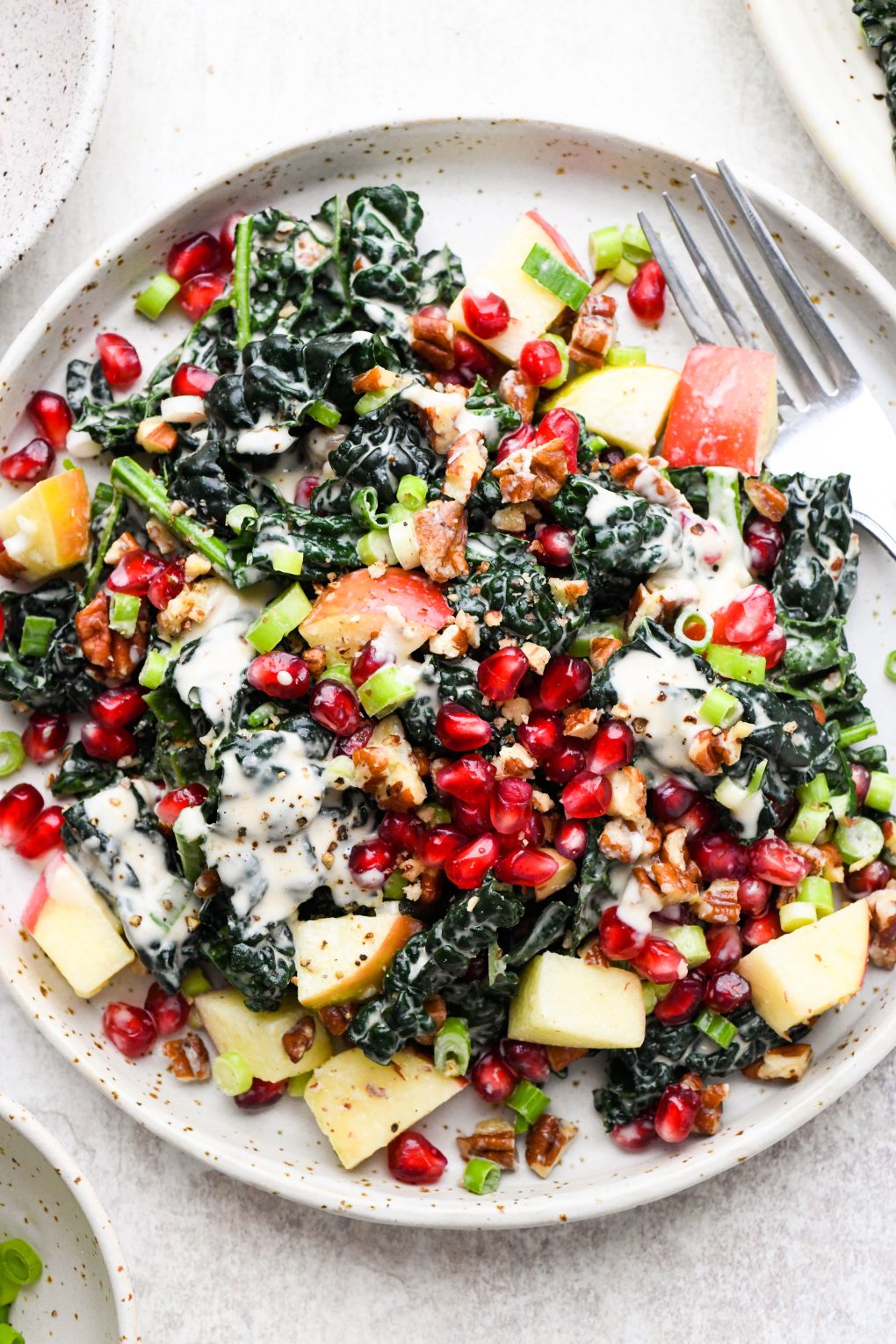 A small salad plate filled with colorful kale apple pomegranate salad with creamy tahini dressing.