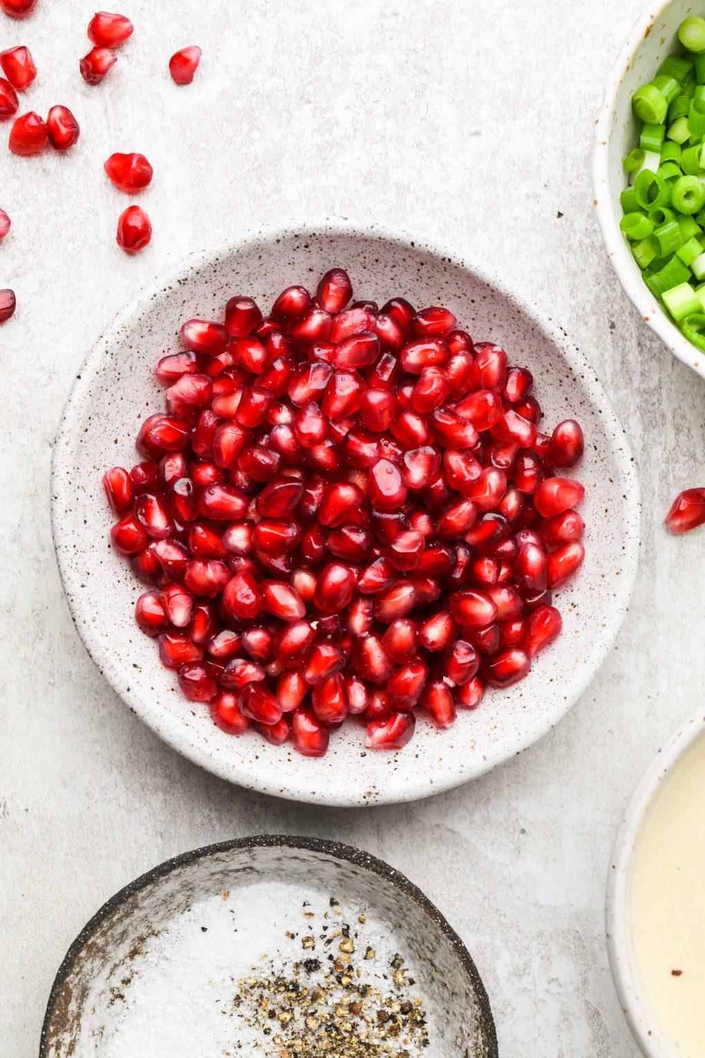 A small speckled bowl filled with bright red pomegranate seeds.