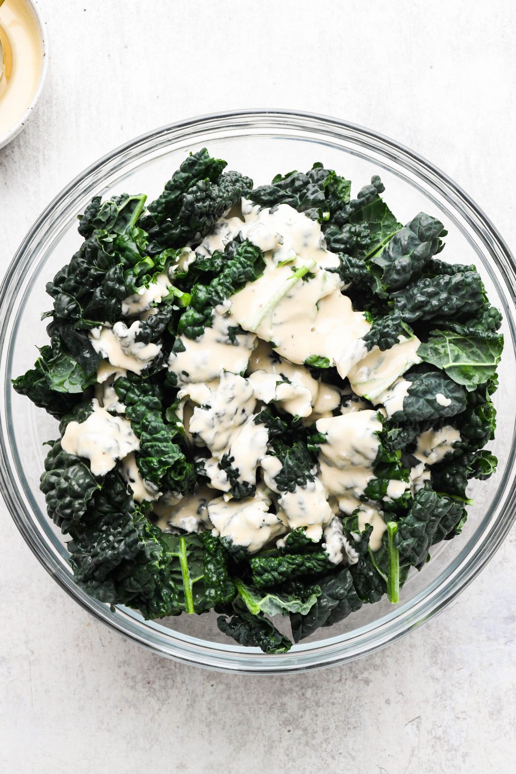 A large bowl filled with raw kale leaves and drizzled with creamy tahini dressing. 