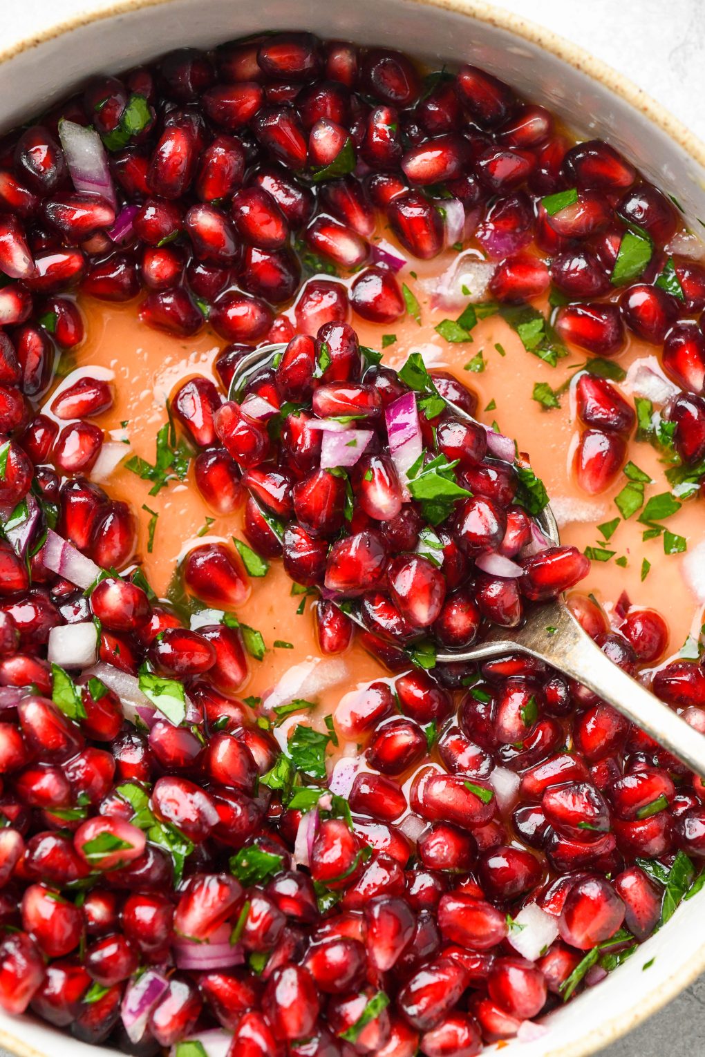 An close up overhead image of a wide shallow bowl of fresh pomegranate relish with diced red onion and parsley. 