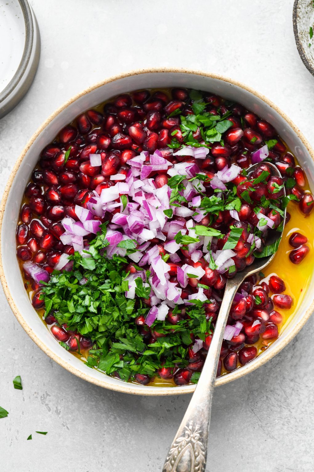 How to make fresh pomegranate relish - a large rimmed bowl with the ingredients for the dressing whisked together and the pomegranate seeds, onions, and parsley on top. 