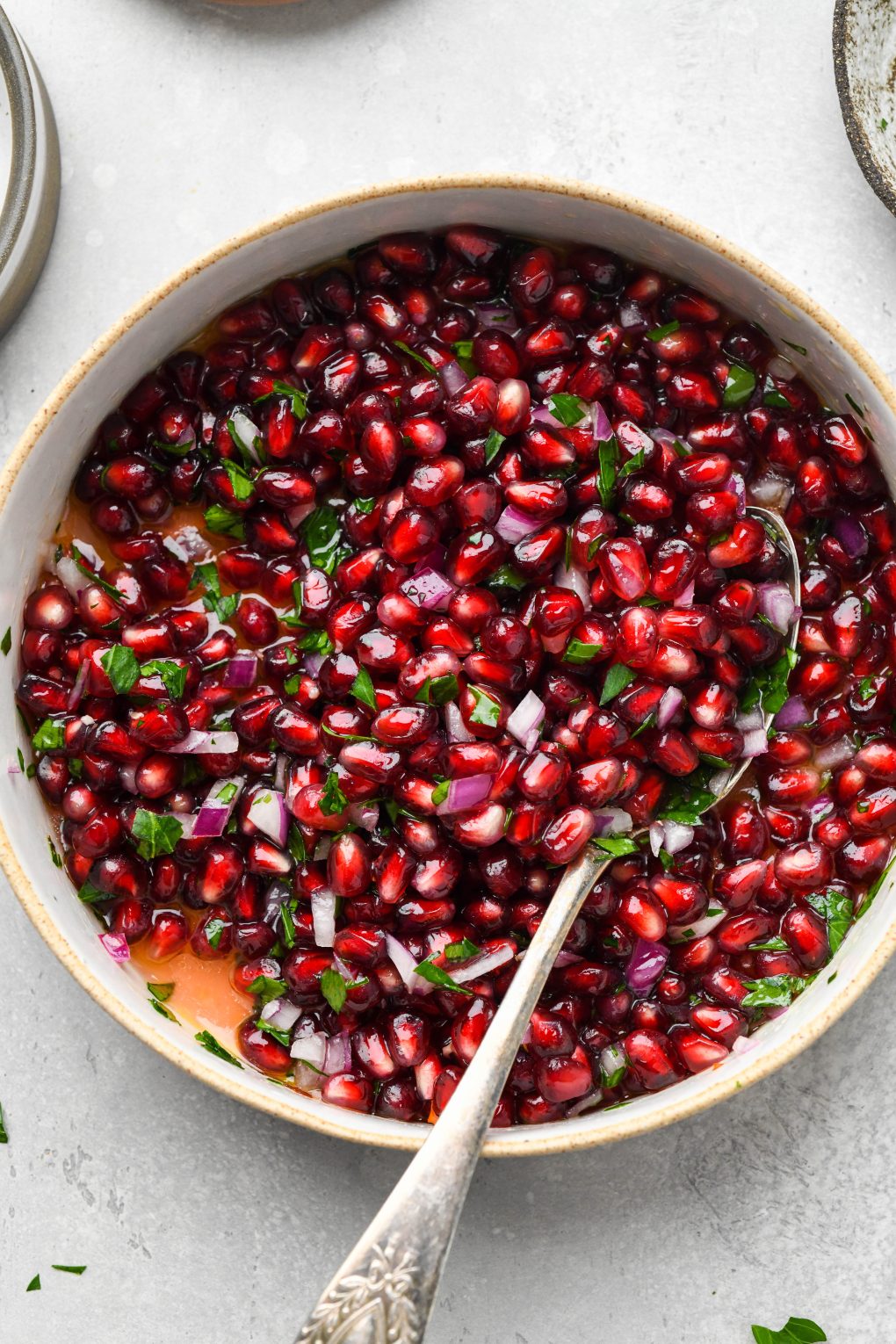 How to make fresh pomegranate relish - An overhead image of a wide shallow bowl of fresh pomegranate relish with diced red onion and parsley. 