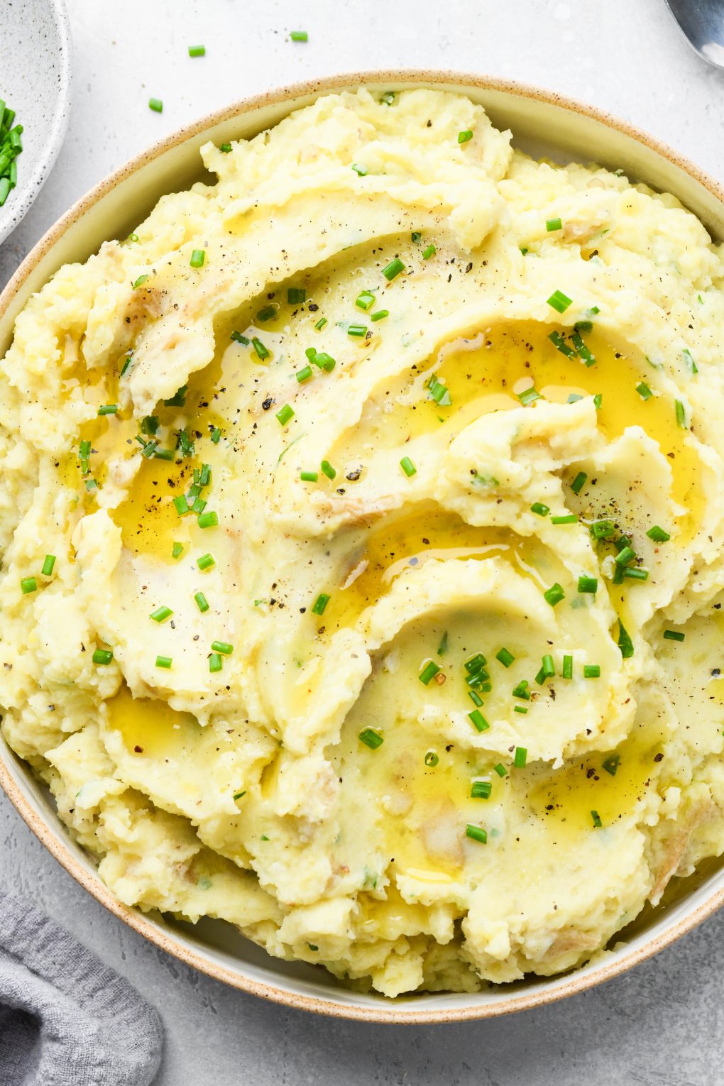 Overhead view of a large bowl filled with swirled creamy Whole30 mashed potatoes topped with melted ghee and chopped chives. 