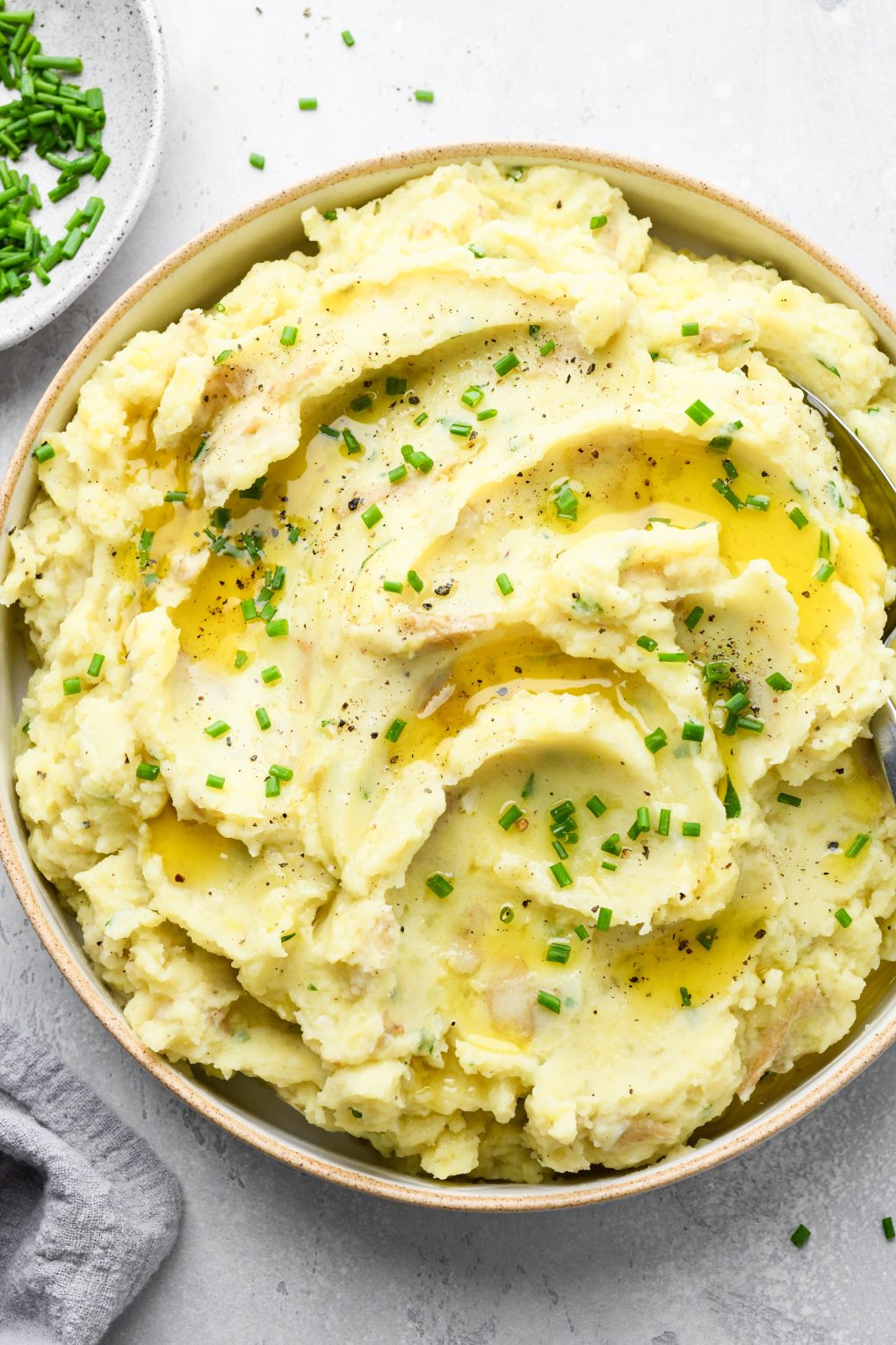 Overhead view of a large bowl filled with swirled creamy Whole30 mashed potatoes topped with melted ghee and chopped chives. 