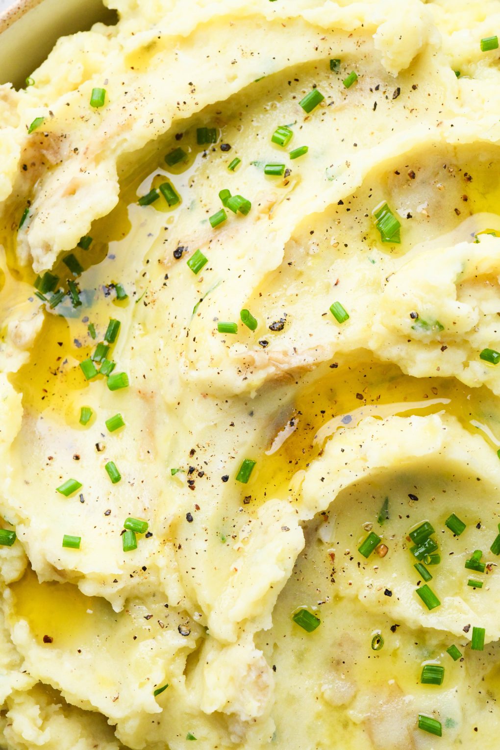 Super close up overhead view of a large bowl filled with swirled creamy Whole30 mashed potatoes topped with melted ghee and chopped chives. 
